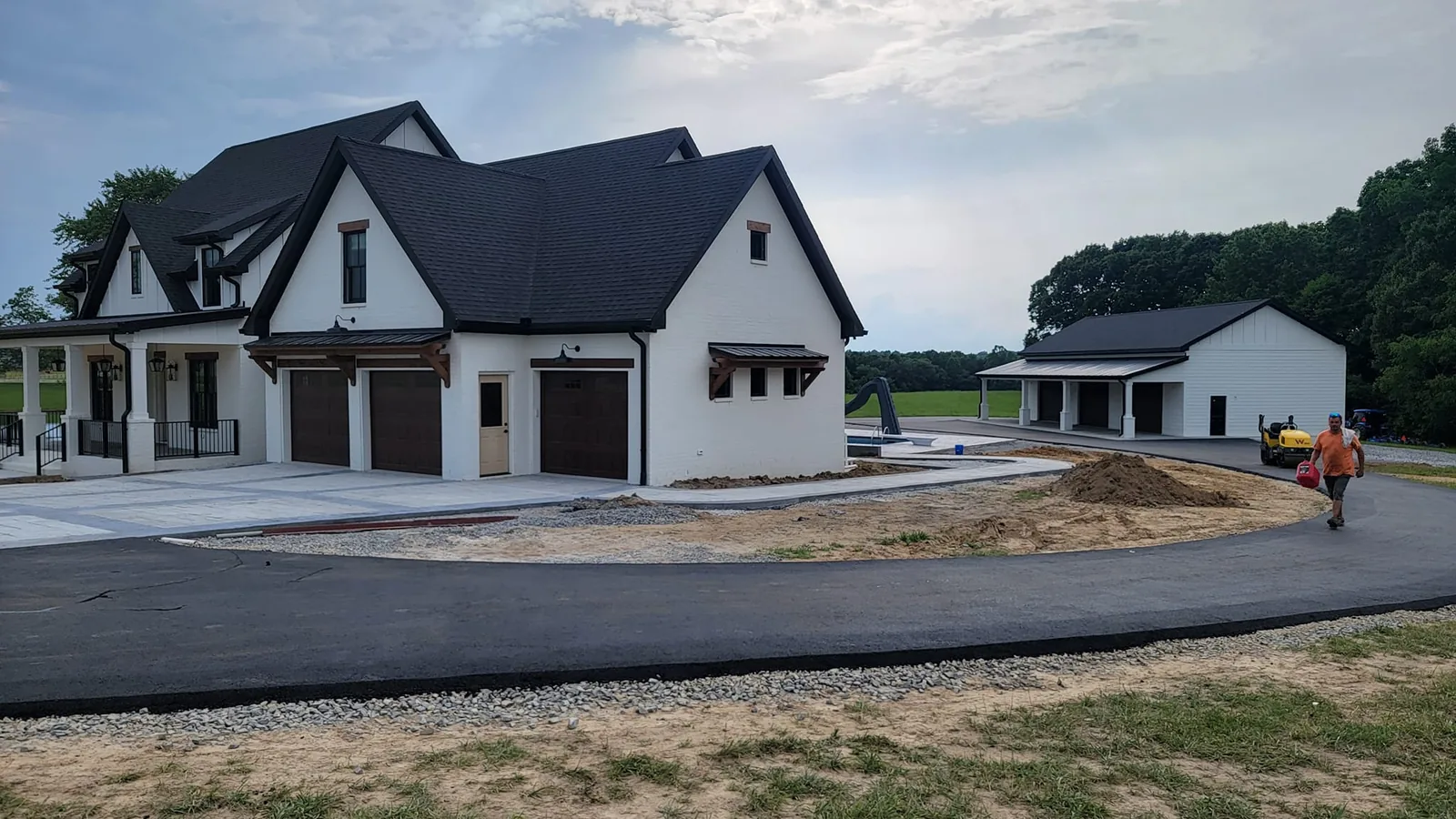 New asphalt driveway paving curving around a white farmhouse and outbuilding
