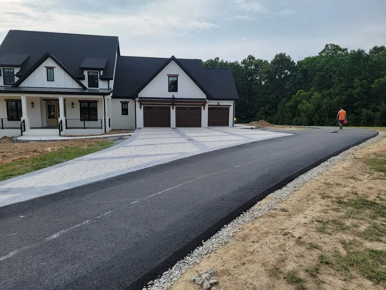 New asphalt driveway paving beside a white farmhouse with a three car garage