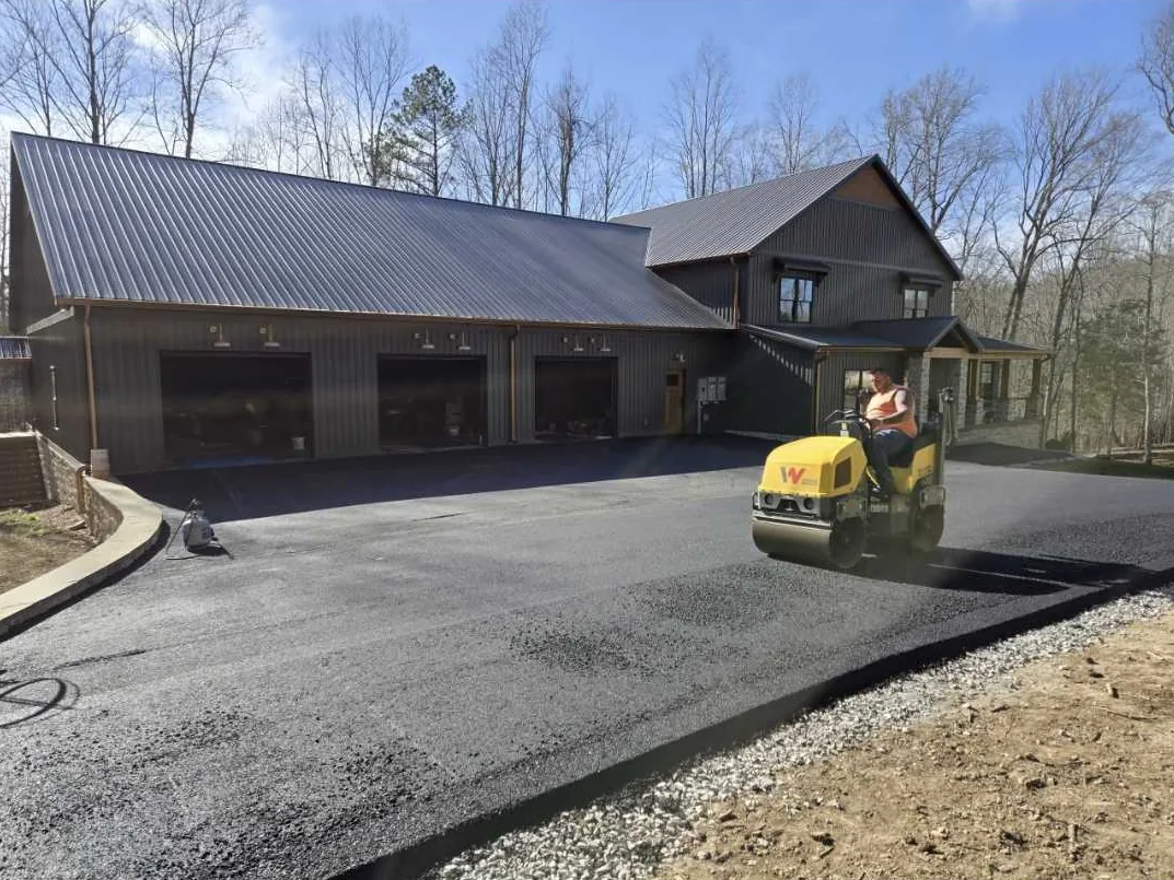 Asphalt driveway paving with a roller compacting fresh hot mix at a metal shop house