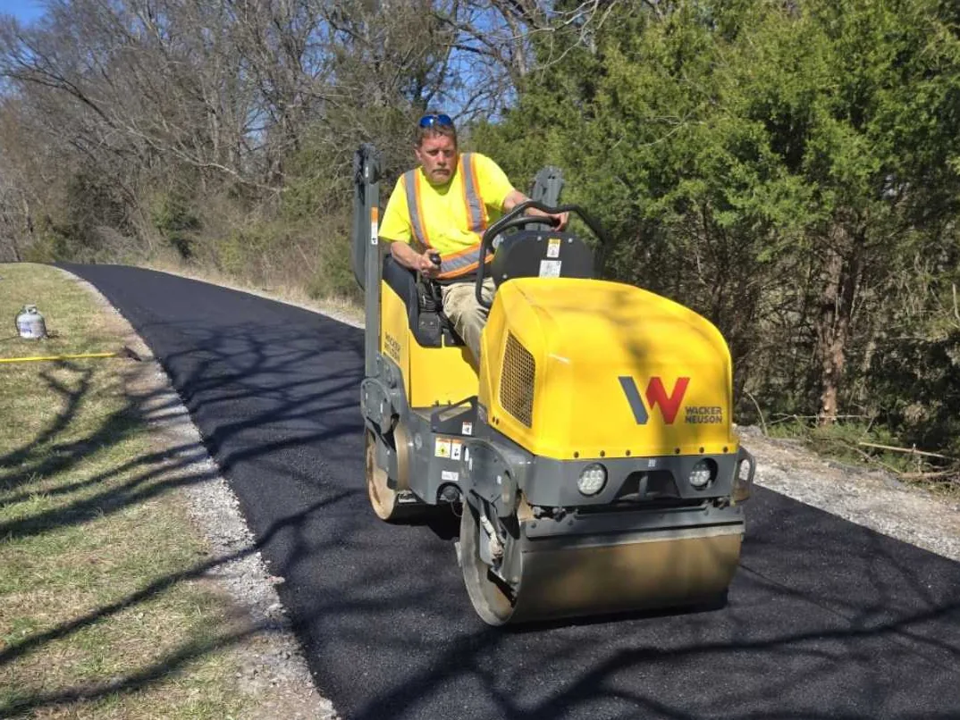 Asphalt driveway paving with a roller operator compacting a fresh asphalt drive