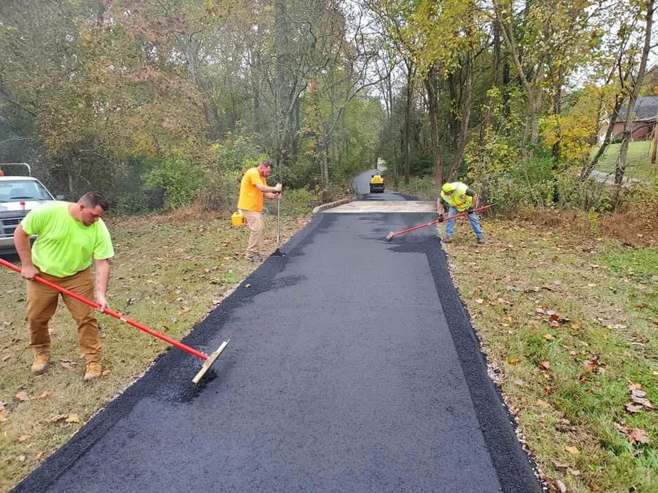 Crew raking hot mix asphalt by hand along a fresh lane, asphalt repair and patching