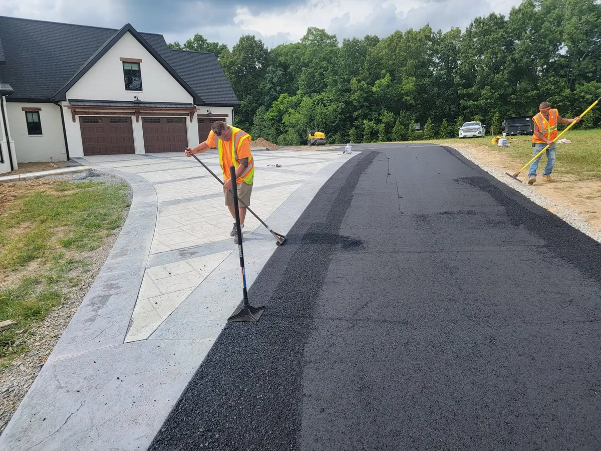 Workers hand raking hot mix where new asphalt meets a concrete apron, asphalt repair