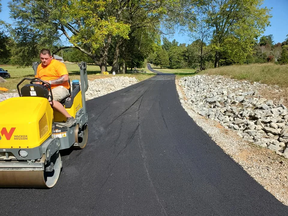 Roller compacting fresh asphalt beside a rock lined shoulder, asphalt repair