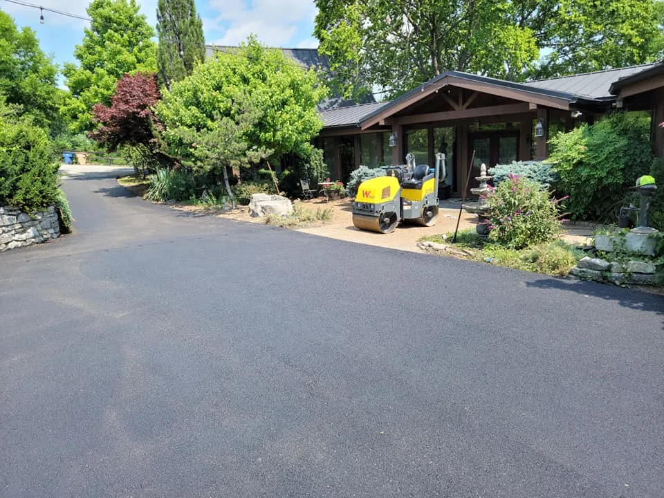 Asphalt resurfacing finished in front of a landscaped home with a roller parked