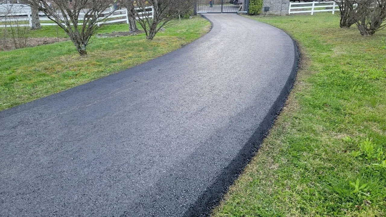 Curving asphalt driveway paving leading to a gate between white fences
