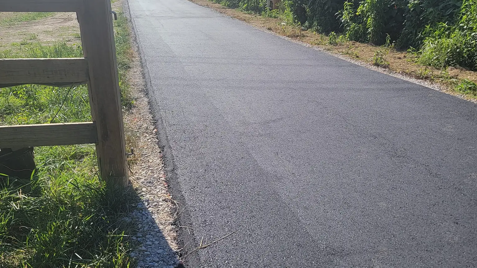 Fresh asphalt lane paving beside a wooden fence post