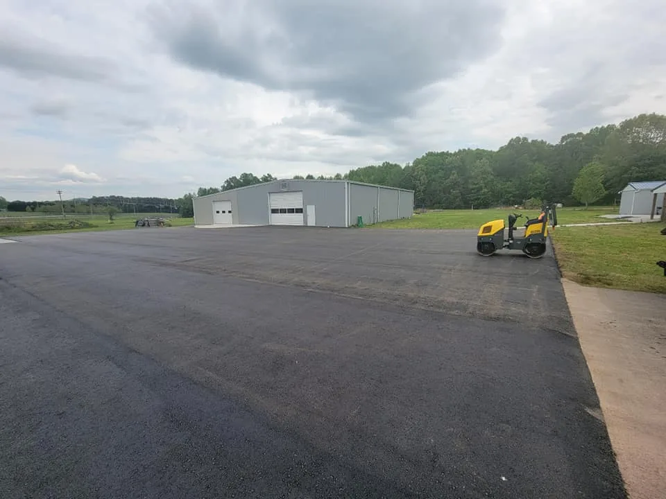 Freshly paved lot at a metal shop building with a roller parked, ready for parking lot striping