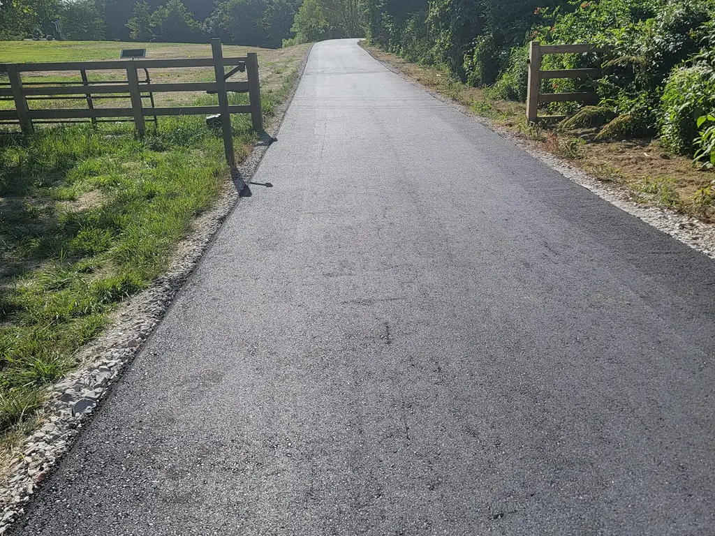 Private road paving on a fresh asphalt lane past a wooden farm gate