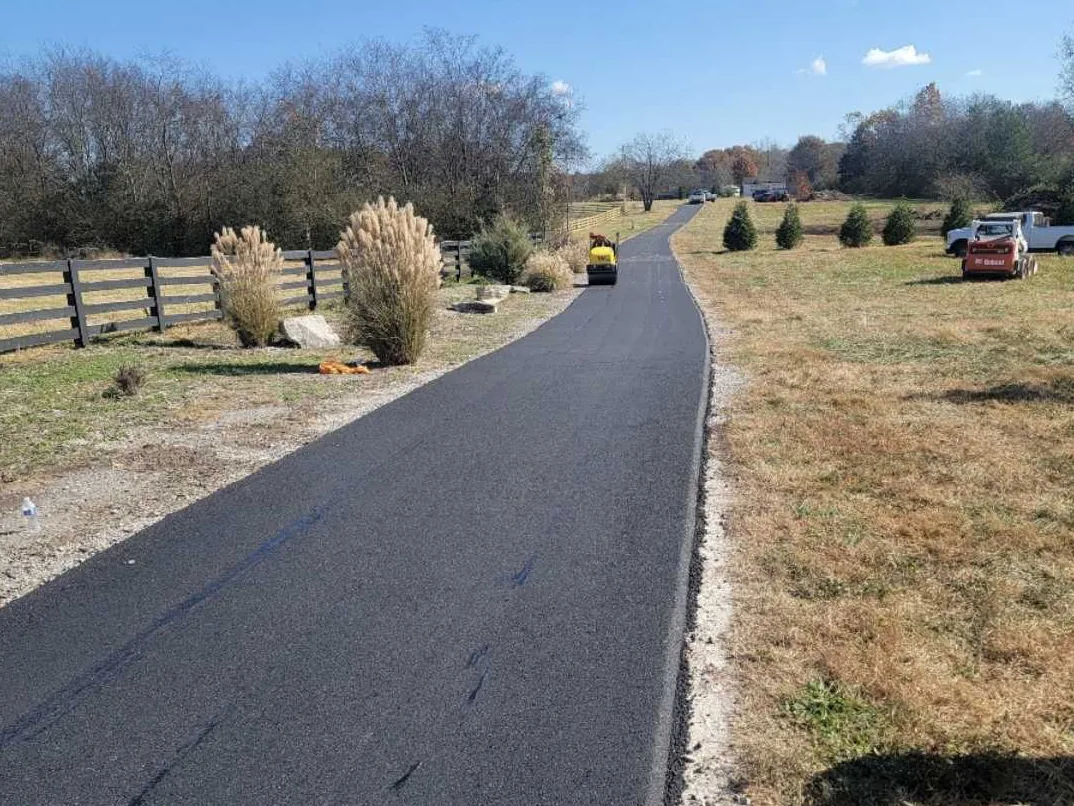 Private road paving on a long rural asphalt lane beside a black board fence