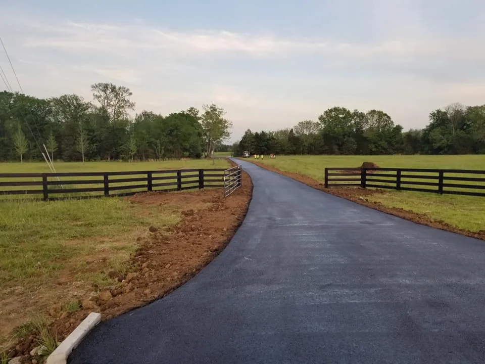Private road paving on a new asphalt farm lane between black horse fences