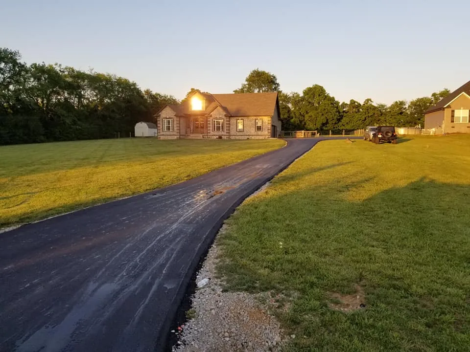Fresh asphalt driveway leading to a brick home at sunset, ready for sealcoating