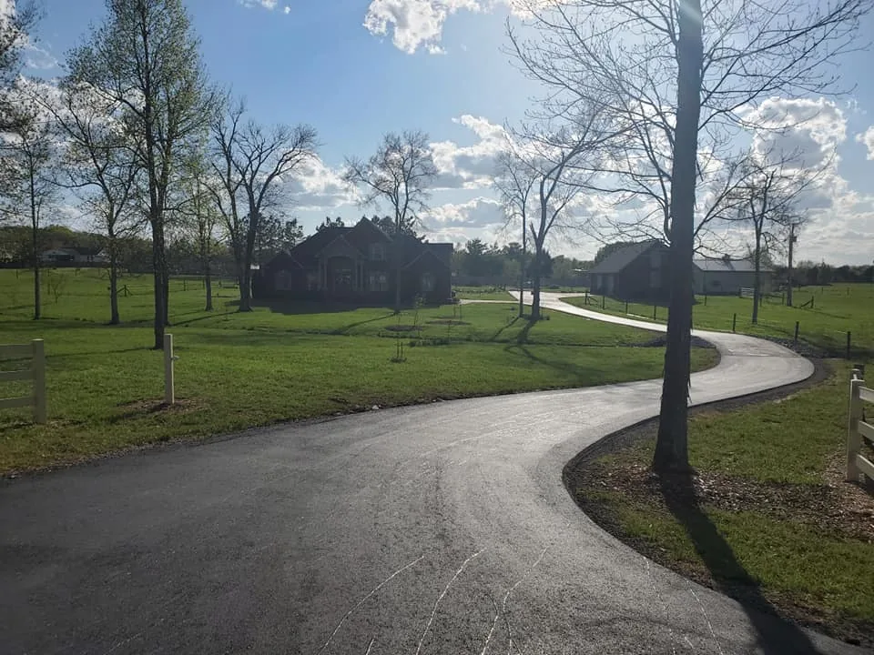 Curving asphalt driveway across a lawn with young trees, ready for sealcoating