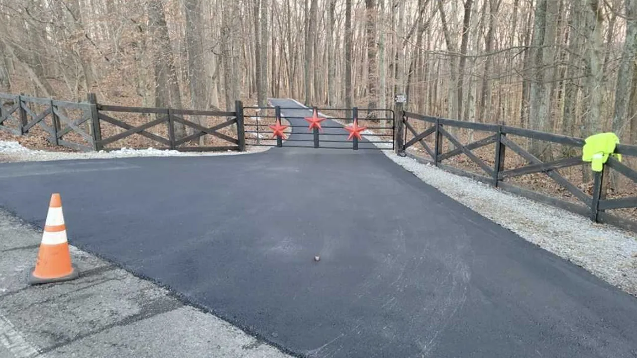 Asphalt paving at the entrance of a gated wooded lane
