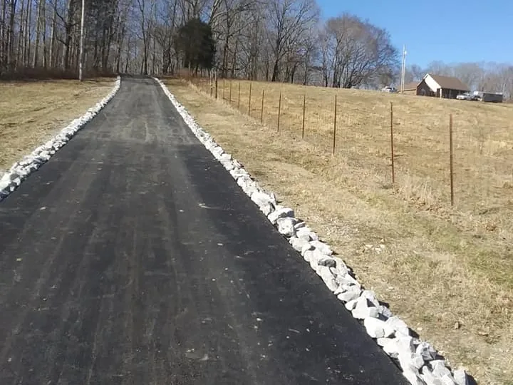Asphalt farm lane edged with white rock along a fenced pasture, a tar and chip alternative