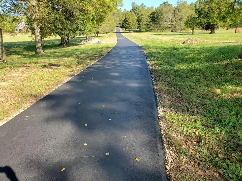 Long hot mix asphalt farm lane through open grass, a tar and chip alternative