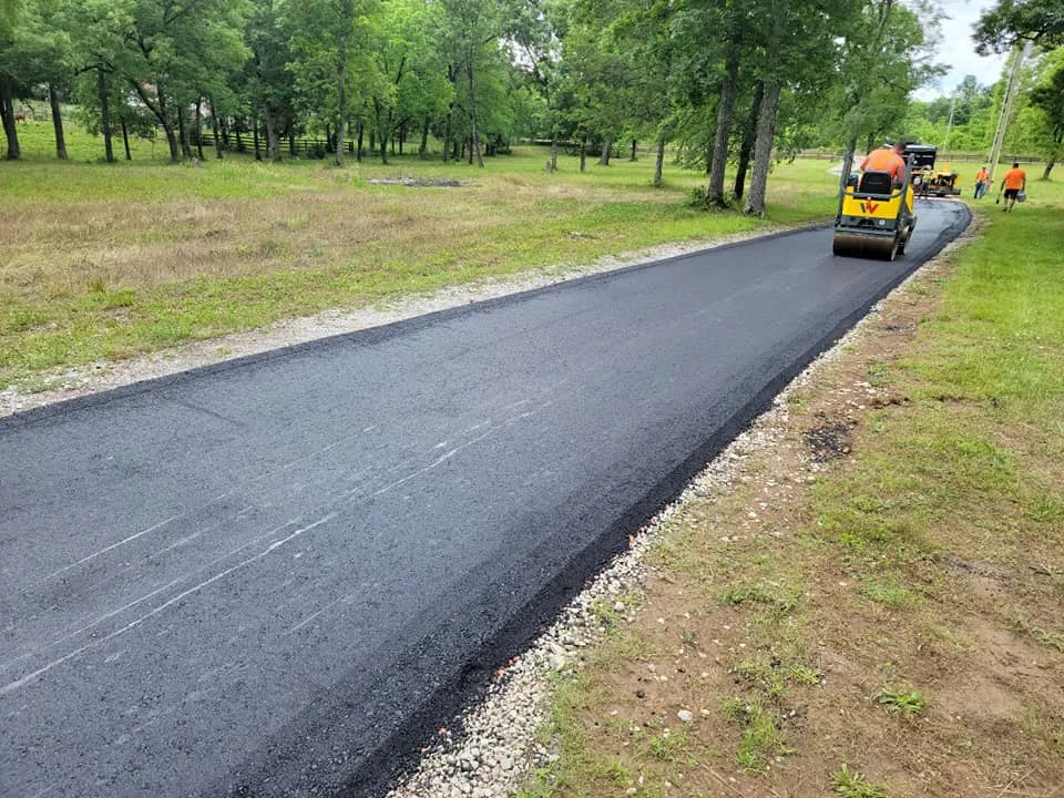 Roller finishing a long asphalt farm lane, a tar and chip alternative